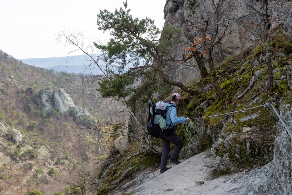 Maca a Markus zostupujú zaistenou cestou nad Durnstain v Rakusku. Markus spí spokojne v nosiči Thule Sapling. Thule Sapling detský turistický nosič