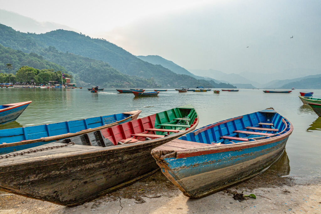 Farebné loďky v popredí, v pozadí džungľa, jazero Phewa, Pokhara