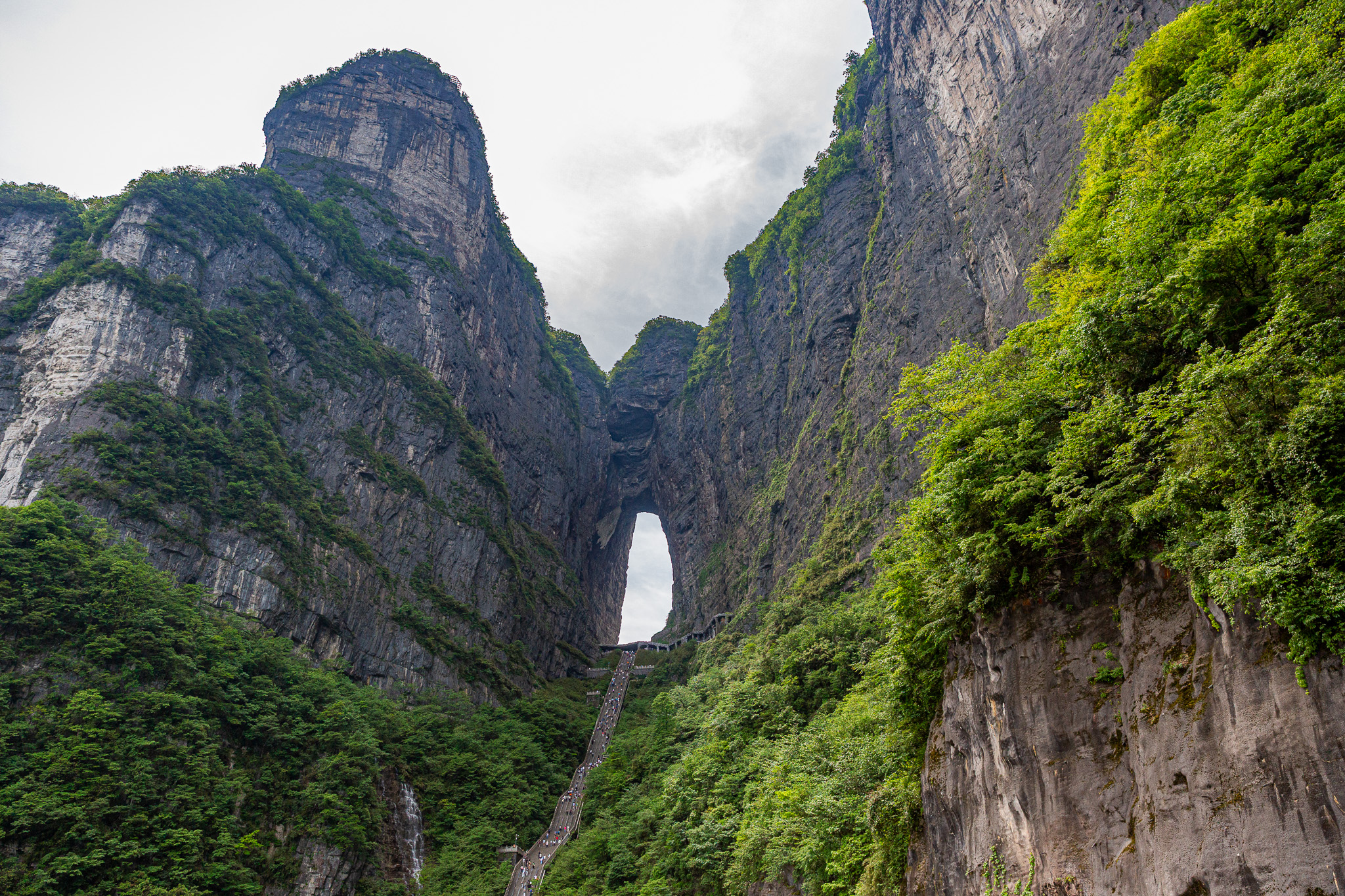 Majestátny skalný masív s ikonickým oknom Nebeská brána a lanovkou v oblasti Tianmen Mountain, Zhangjiajie, Čína.