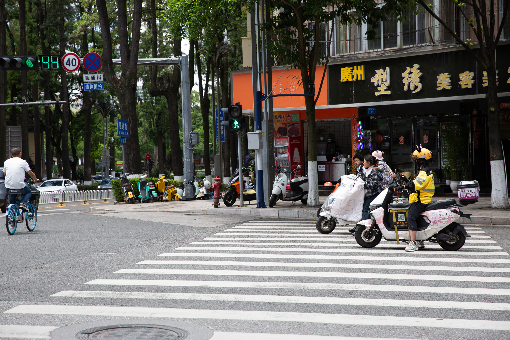 Skútre a cyklisti na priechode pre chodcov v uliciach mesta Kunming, Čína.