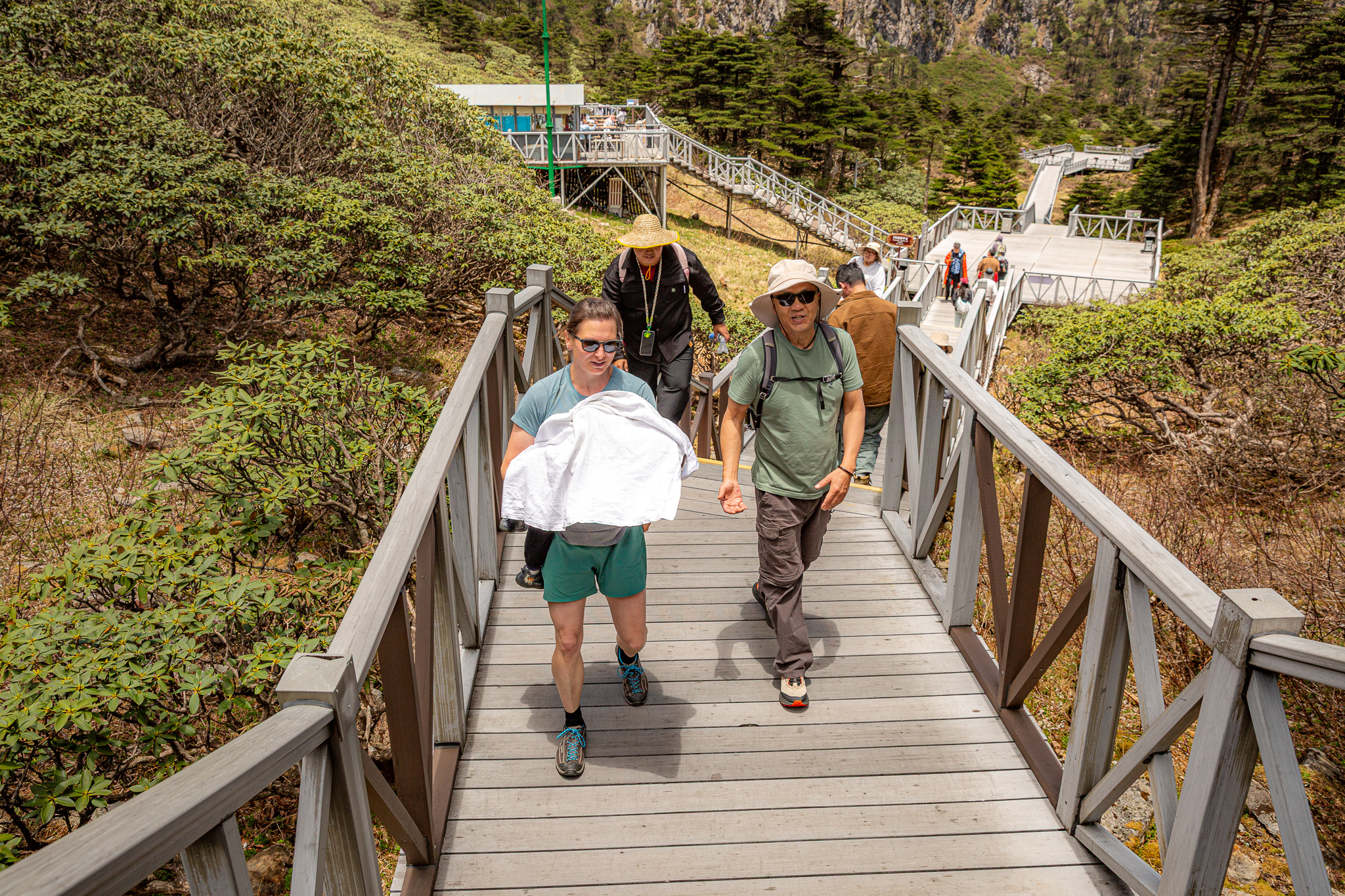 Žena nesúca spiace dieťa v náručí, pričom kráča po schodoch smerom k hornej stanici lanovky na hore Cangshan vo výške niečo pod 4 000 m n.m. Dali, Yunnan, Čína