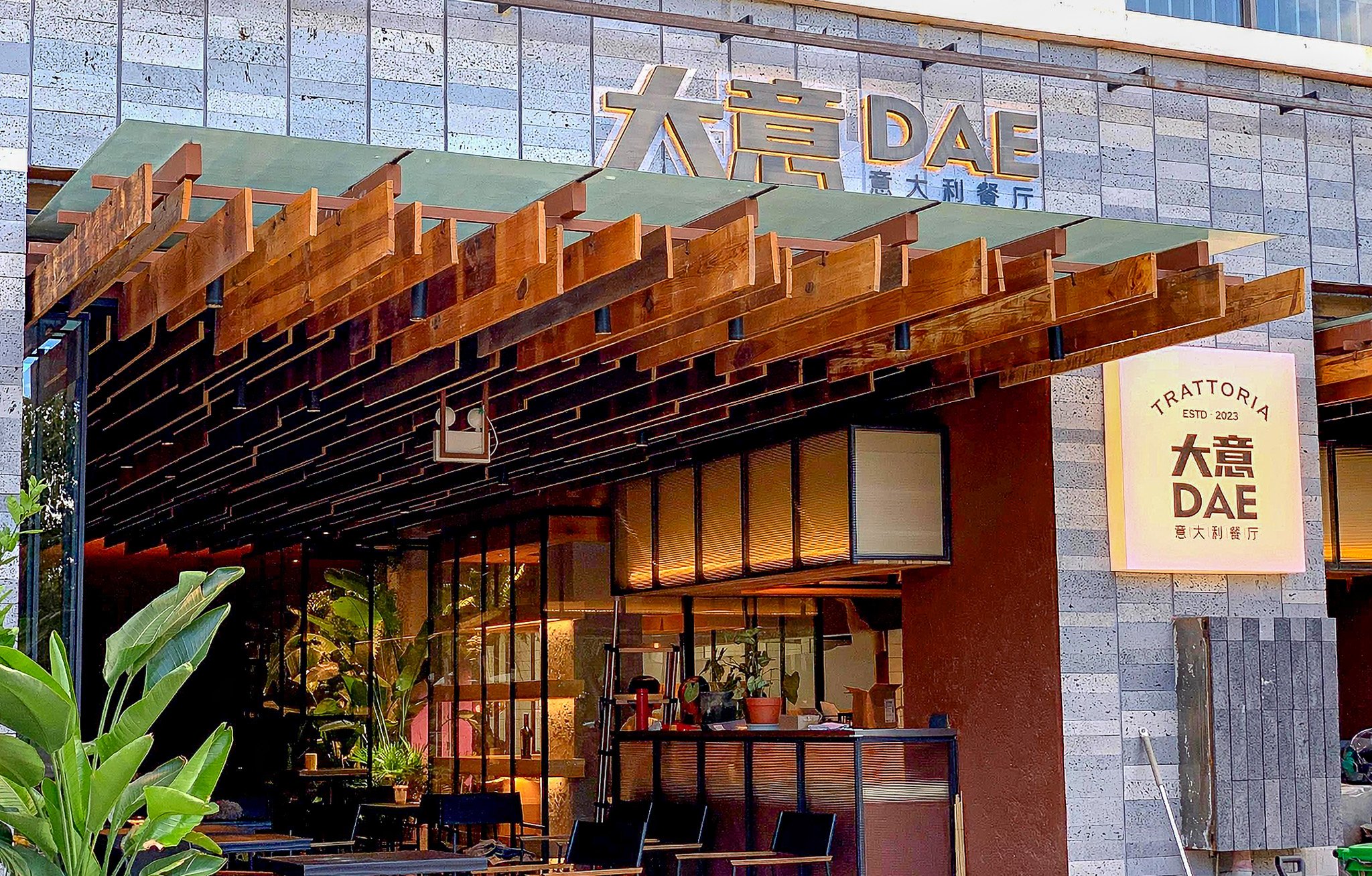 Štýlová talianska reštaurácia 大意 DAE Trattoria, ktorá sa nachádza v známej umelecko-kreatívnej štvrti Zuoan Gaodi (Left Bank Highlands) v Dali. Názov reštaurácie v sebe nesie vtipnú slovnú hračku: Čínsky názov 大意 (Dàyì) v preklade znamená „neopatrný“ alebo „ležérny/uvolnený“. Zároveň však jeho výslovnosť znie takmer identicky ako čínske slovo pre Taliansko – 意大利 (Yìdàlì). Tento podnik patrí medzi veľmi populárne a vysoko hodnotené západné reštaurácie v celej oblasti. Návštevníci z Dianpingu (čínska obdoba Tripadvisoru) a cestovateľských komunít tu najviac vyzdvihujú autentickú pizzu z kamennej pece, hľuzovkové špeciality, burratu s pečenou tekvicou a skvelé steaky z hovädzieho mäsa Wagyu. Architektúra s výrazným dreveným podhľadom a otvorenou terasou skvelo zapadá do uvoľnenej a modernej atmosféry, ktorou je Dali medzi cestovateľmi známe. Yunnan, Čína