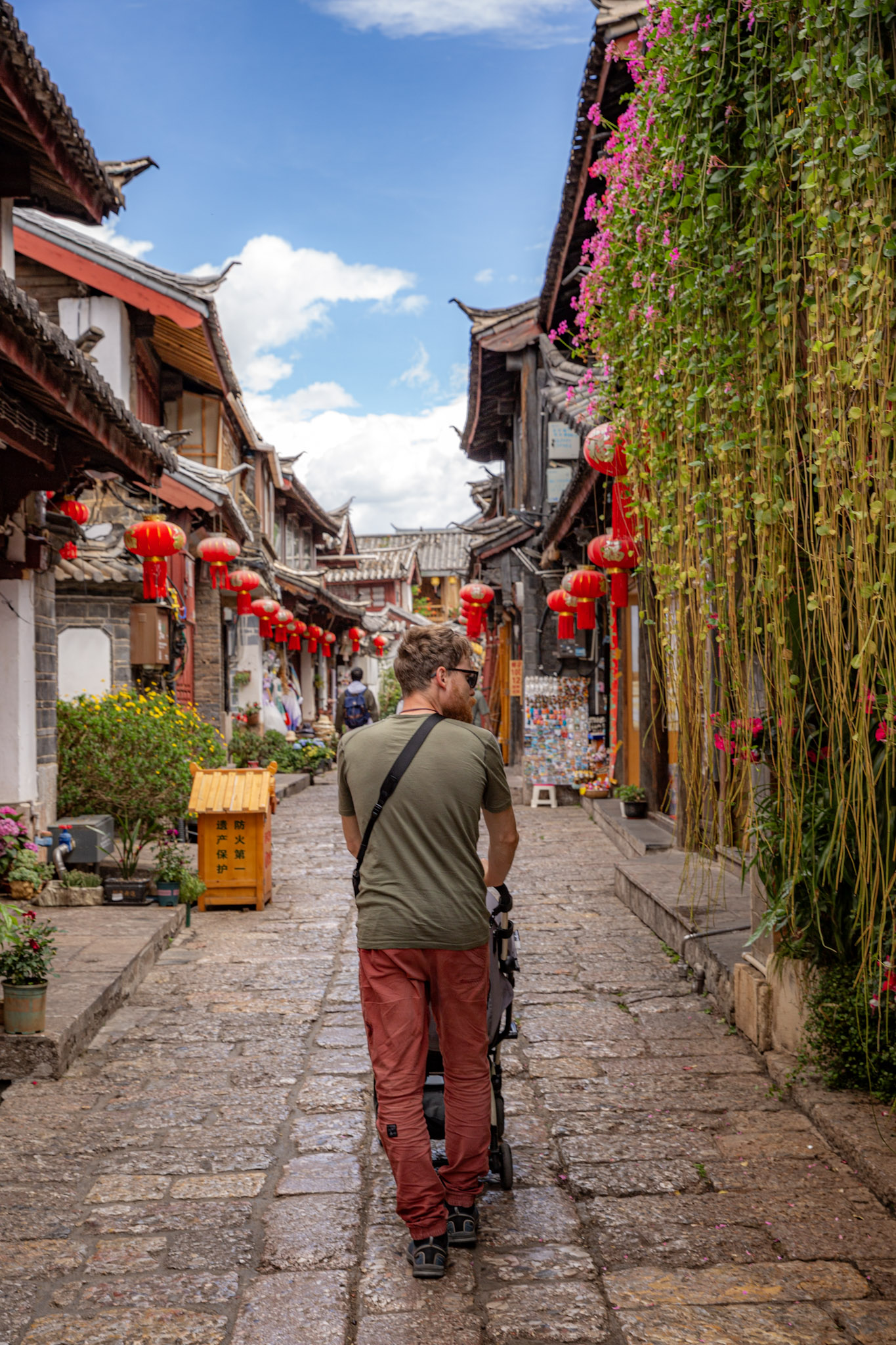Muž s kočíkom prechádza historickou uličkou s lampiónmi v čínskom meste Lijiang.