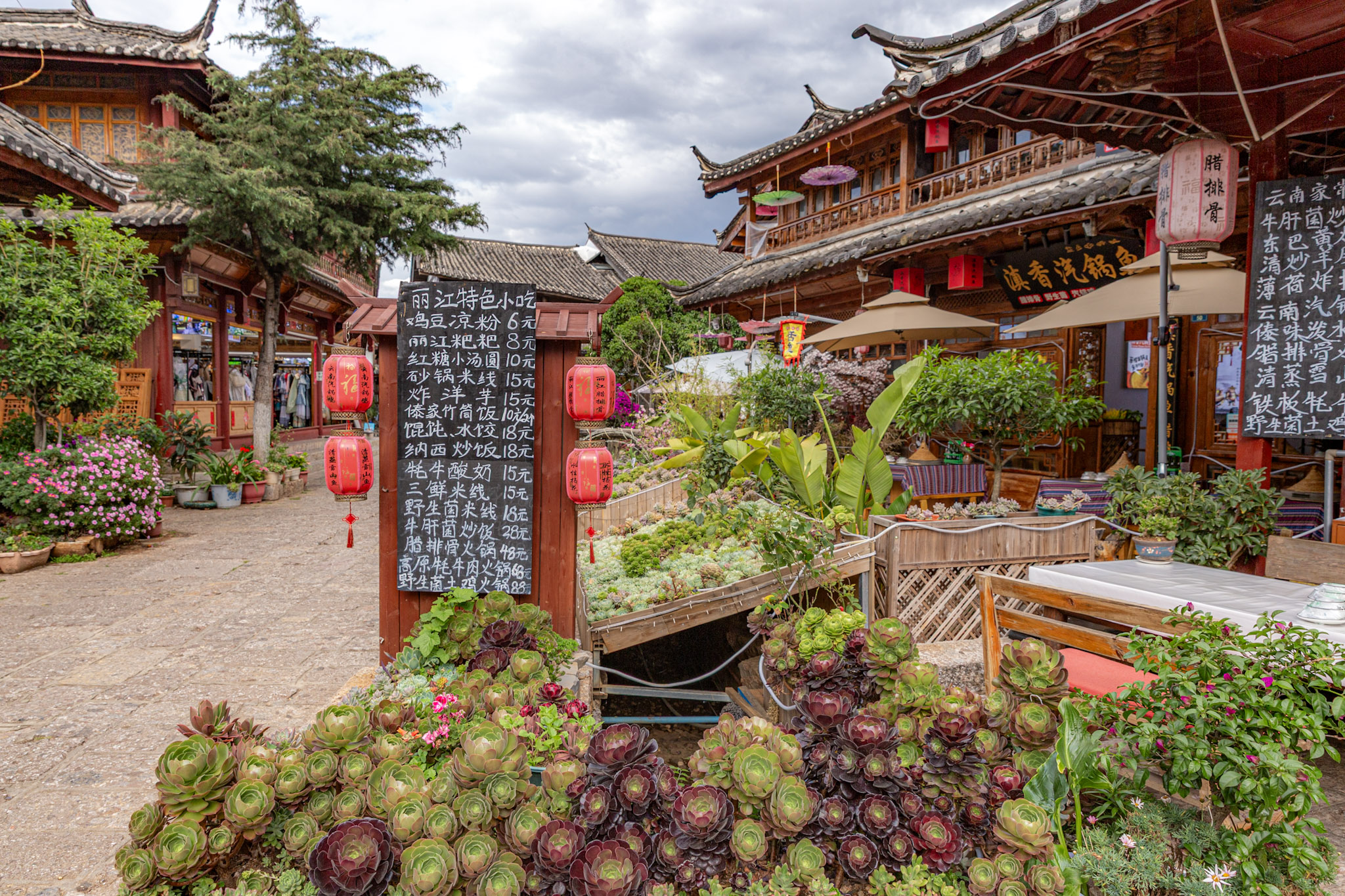 Drevená ponuková tabuľa s čínskym písmom a červenými lampiónmi pred tradičnou reštauráciou v meste Lijiang.