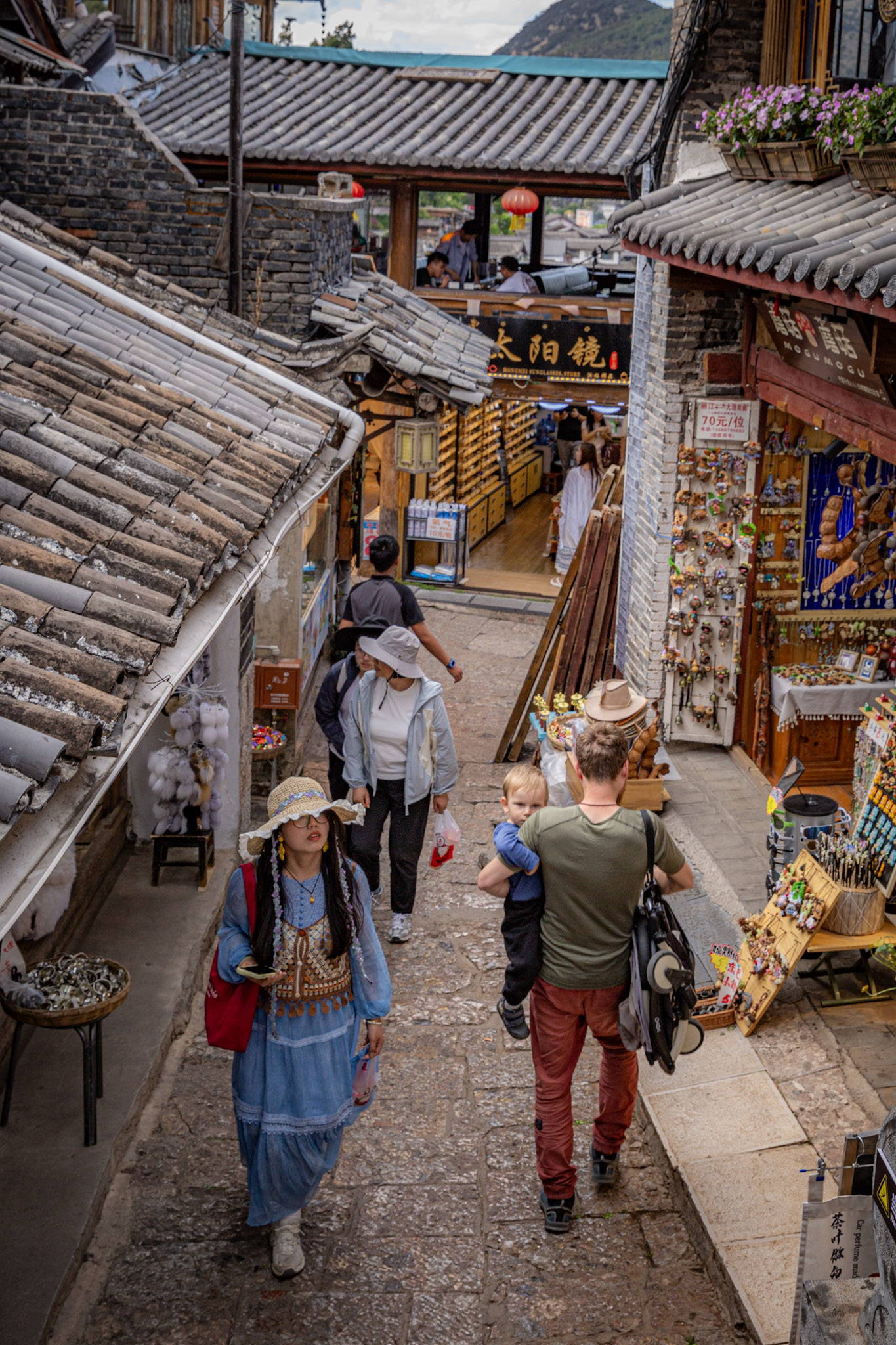 Muž s dieťaťom na rukách kráča po schodoch rušnej historickej uličky v čínskom meste Lijiang.