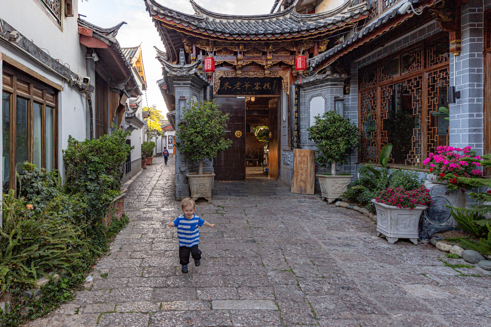 Malé dieťa v modro-bielom pásikavom tričku beží po historickej kamenej uličke v starom meste Lijiang v Číne.