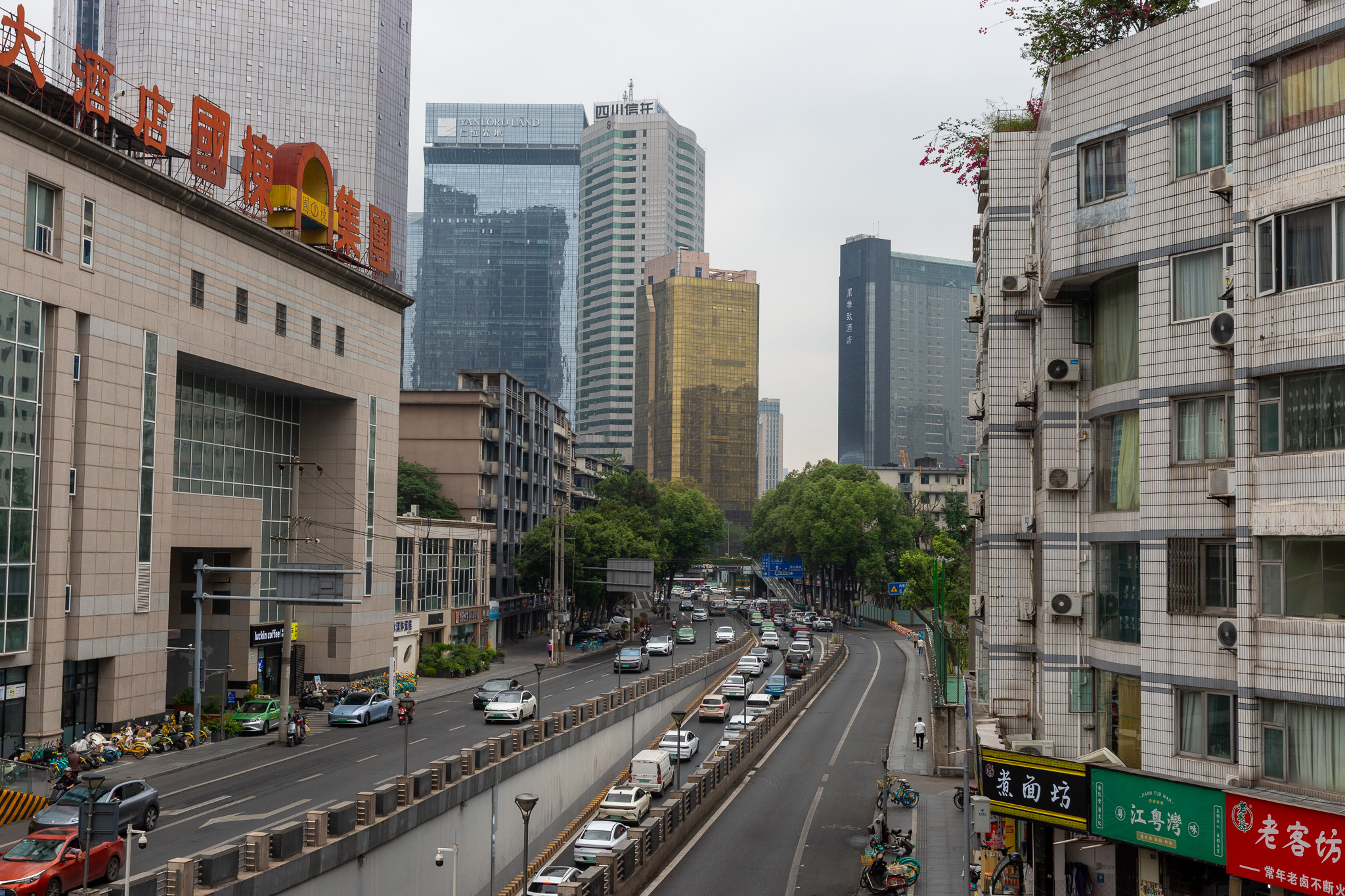 Ulica s množstvom áut, lemovaná budovami a mrakodrapmi v Chengdu.