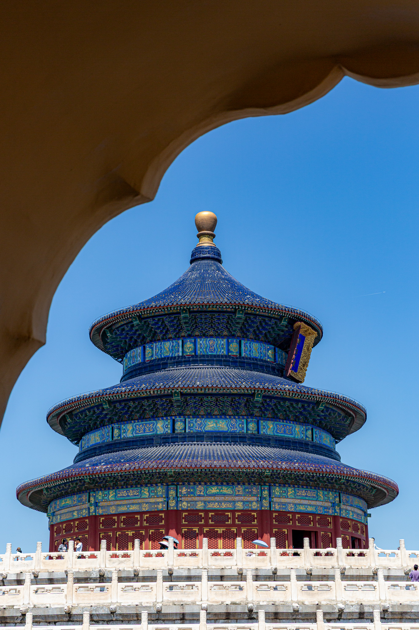 Modrý tradičný taoistický chrám kruhového tvaru Temple of Heaven, v pozadí modrá obloha a v popredí tri poschodia s bielym múrom. Peking