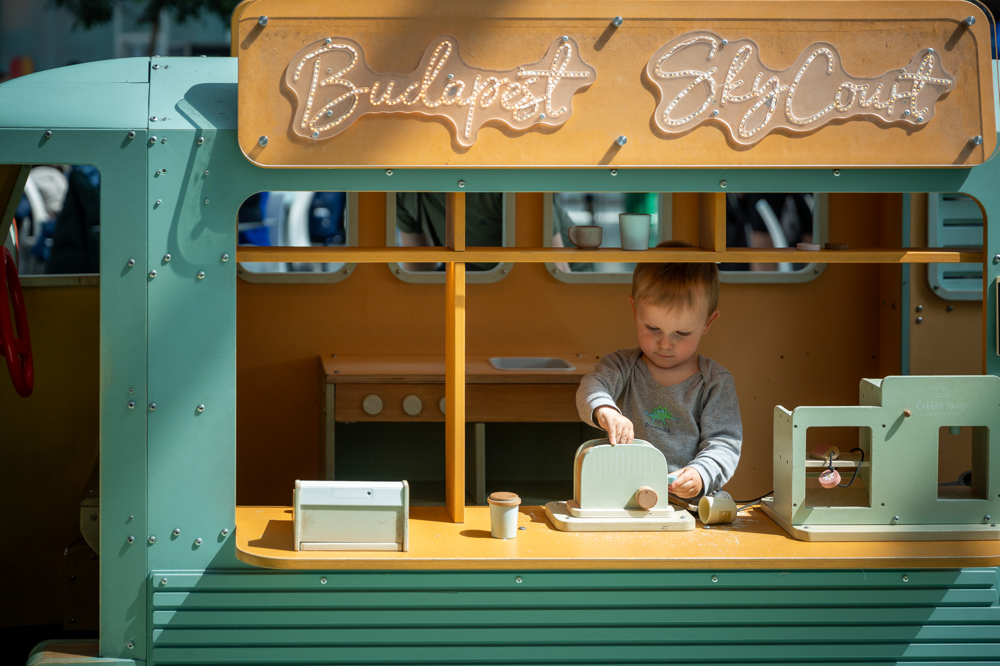 Batoľa v detskom drevenom food trucku „Budapest Sky Court“ sa hrá s hračkárskym hriankovačom.