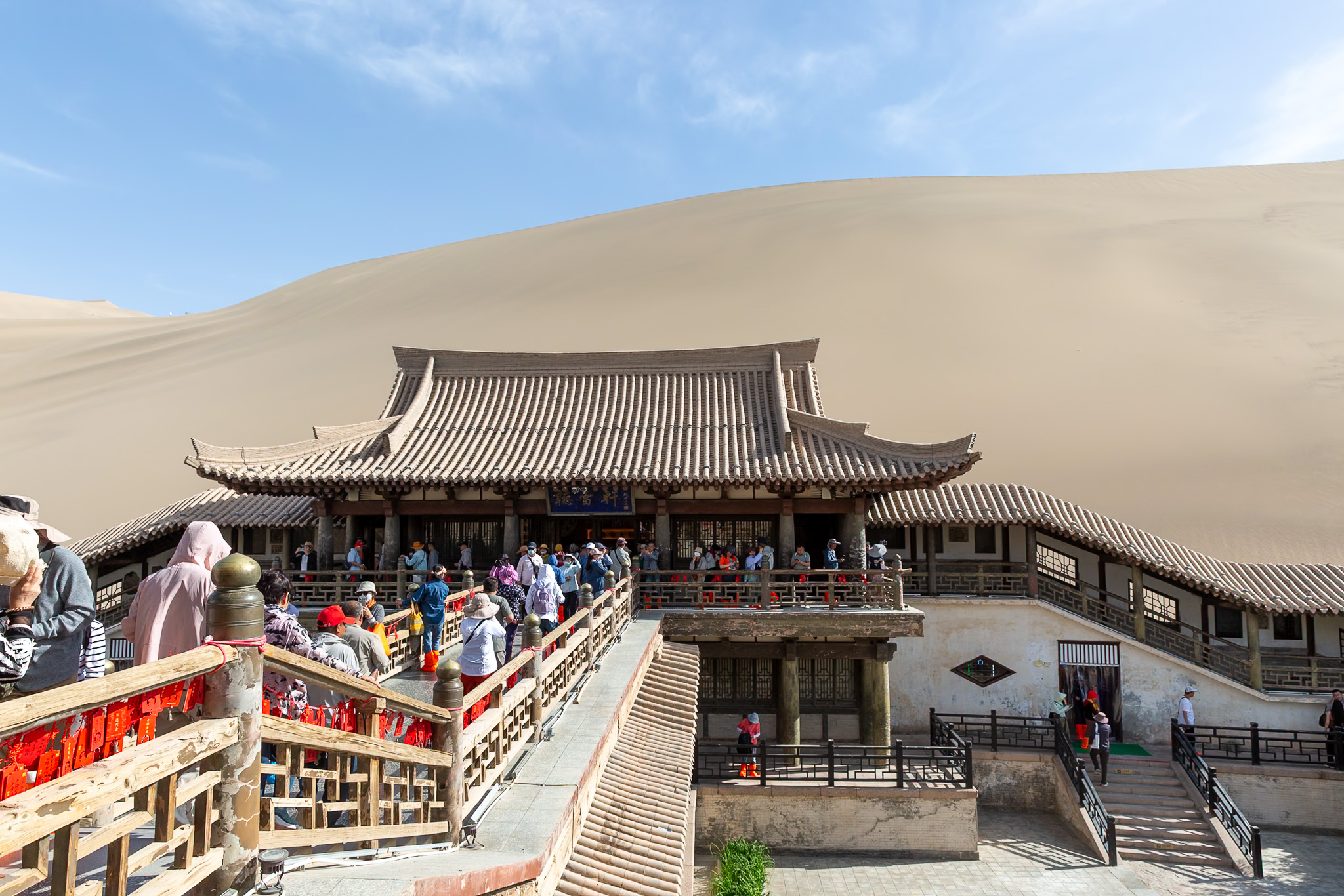 Turisti na terasách tradičného čínskeho chrámu Yueya Spring priamo pod masívnou piesočnou dunou v oáze Dunhuang.