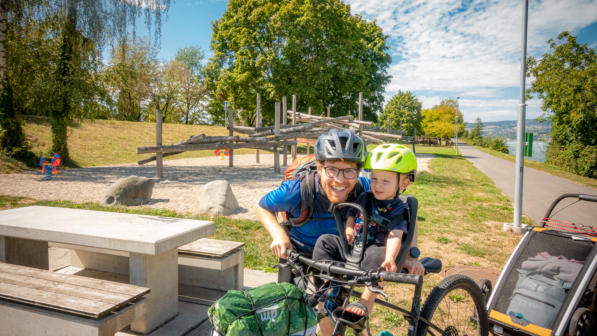 Cyklista so synom v cyklosedačke na detskom ihrisku sa smejú
